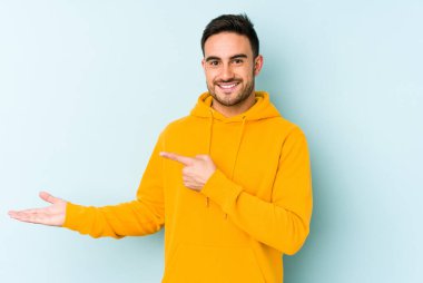 Kafkasyalı genç adam mavi arka planda izole edilmiş. Elinde palmiye ağacının bir kopyası olduğu için heyecanlı..