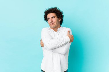 Genç, kıvırcık, olgun bir adam zarif bir gömlek giyiyor, sarılıyor, kaygısız gülümsüyor ve mutlu..