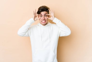 Beyazlı genç bir adam bej arka planda izole edilmiş. Başarı fırsatı bulmak için gözlerini açık tutuyor..