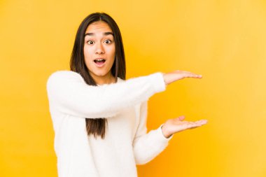 Sarı arka planda izole edilmiş genç bir kadın elleri arasında bir kopya alanı tutarken şok ve hayret içinde..