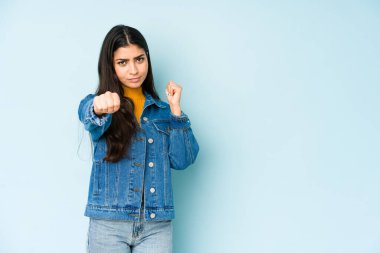 Genç Hintli bir kadın mavi arka planda izole edilmiş. Bir tartışma yüzünden yumruk, öfke, kavga, boks atıyor..