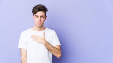 Mor arka planda izole edilmiş genç beyaz adam yemin ediyor, elini göğsüne koyuyor..