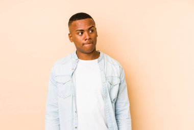Bej arka planda izole edilmiş genç latin adam kafası karışmış, şüpheli ve güvensiz hissediyor..
