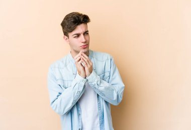 Kafkasyalı genç bir adam, bej arka planda izole edilmiş bir plan kuruyor, bir fikir kuruyor..