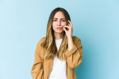 Mavi arka planda izole edilmiş genç beyaz kadın parmakları dudaklarında bir sır saklıyor..