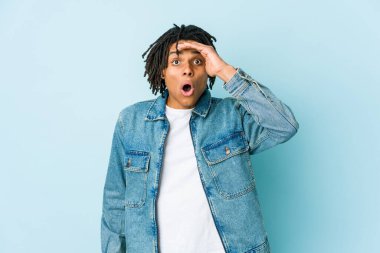 Kot ceket giyen genç siyahi adam çok uzaklara bakıyor ve elini alnına koyuyor..