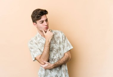 Beyazlı genç adam bej arka planda izole edilmiş şüpheli ve şüpheci bir ifadeyle yana bakıyor..