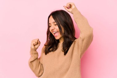 Latin kökenli genç bir kadın özel bir günü kutluyor, atlıyor ve enerji ile kollarını kaldırıyor..