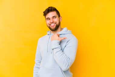 Kafkasyalı genç adam sarı arka planda izole edilmiş, başparmak uzakta, gülüyor ve kaygısız..