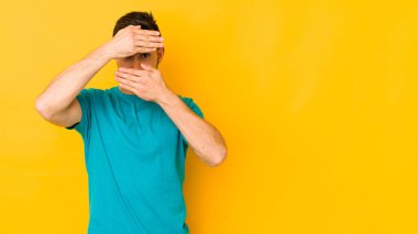 Genç, beyaz bir adam sarı bir alanda izole edilmiş. Kameraya parmaklarıyla göz kırpıyor. Yüzünü kapatmaktan utanıyor..
