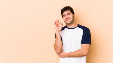 Bej arka planda izole edilmiş genç bir adam bir göz kırptı ve elleriyle iyi bir jest yaptı..