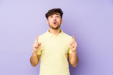Mor arka planda izole edilmiş genç bir Arap adam ağzı açık bir şekilde üst tarafı işaret ediyor..