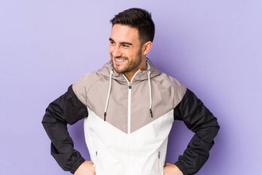 Mor arka planda izole edilmiş genç beyaz adam mutlu bir şekilde gülüyor ve ellerini karnının üstünde tutarak eğleniyor..