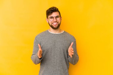 Sarı arka planda izole edilmiş genç beyaz adam iki eliyle bir şey tutuyor, ürün sunumu..