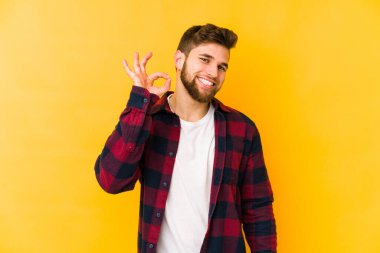 Sarı arka planda izole edilmiş genç beyaz bir adam bir göz kırptı ve elleriyle iyi bir jest yaptı..