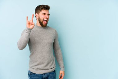 Mavi arka planda izole edilmiş genç beyaz adam boynuzlarını devrim konsepti olarak gösteriyor..