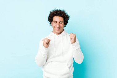 Genç sporcu mavi bir arka plana karşı yumruğunu kaldırıyor, mutlu ve başarılı hissediyor. Zafer konsepti.