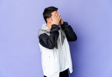 Mor arka planda izole edilmiş genç beyaz adam elleriyle gözlerini kapatmaktan korkuyor..