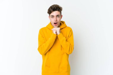 Beyaz arka planda izole edilmiş genç beyaz bir adam şans için dua ediyor, şaşırmış ve ağzını açıp önüne bakıyor..