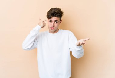 Beyazlı genç bir adam bej arka planda izole edilmiş ve elinde bir ürün var..