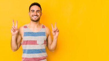 Sarı fırında izole edilmiş genç beyaz adam zafer işareti gösteriyor ve gülümsüyor..