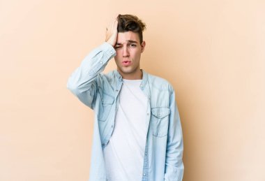 Beyaz tenli genç adam bej arka planda izole edilmiş bir şekilde bir şey unutuyor. Alnına avuç içi ve kapalı gözlerle vuruyor..