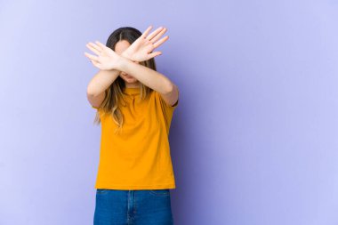 Mor arka planda izole genç beyaz kadın iki kolu çapraz tutuyor, inkar kavramı.