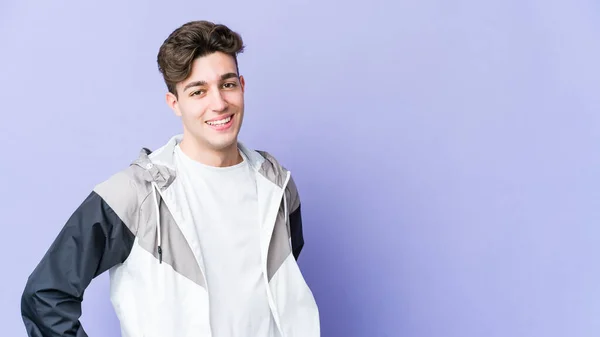 Young caucasian man isolated on purple background confident keeping hands on hips.