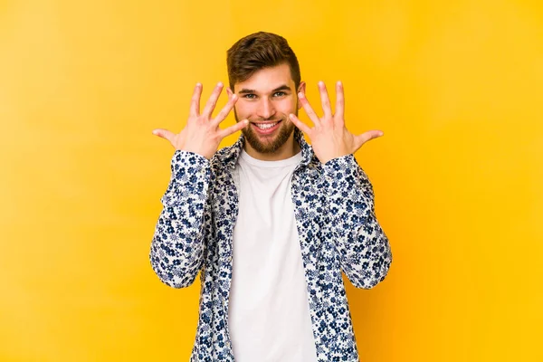 Sarı arka planda izole edilmiş genç beyaz adam on numarayı elleriyle gösteriyor..