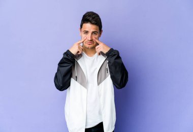 Mor arka planda izole edilmiş genç beyaz bir adam ağlıyor, bir şeyden memnun değil, acı ve kafa karışıklığı konsepti..