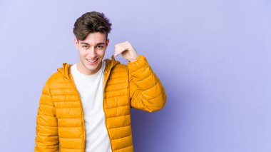 Mor arka planda izole olmuş genç beyaz bir adam bir şeye gülüyor, elleriyle ağzını kapatıyor..