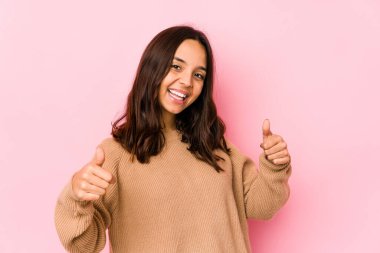 Latin kökenli genç bir kadın kendini soyutlamış. İki parmağını da kaldırmış, gülümsüyor ve kendinden emin..