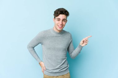 Mavi arka planda izole edilmiş genç beyaz adam işaret parmağıyla işaret ederek gülümsüyor..