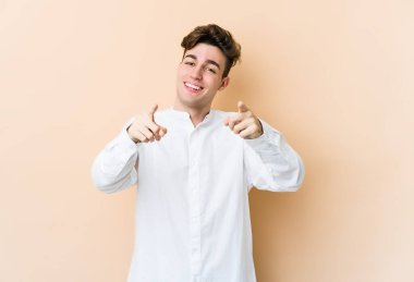 Beyaz tenli genç adam bej arka planda izole edilmiş. Önü işaret eden neşeli gülümsemeler..