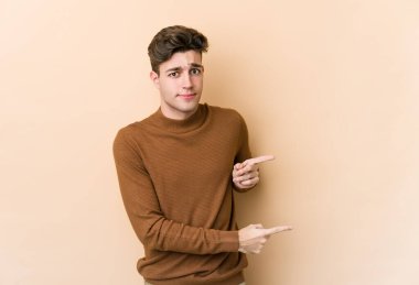 Beyazların arka planında izole edilmiş genç beyaz adam işaret parmağıyla fotokopi alanını işaret ederek şok oldu..