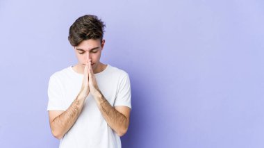 Mor arka planda izole edilmiş genç beyaz adam dua ediyor, bağlılık gösteriyor, dindar biri ilahi ilham arıyor..