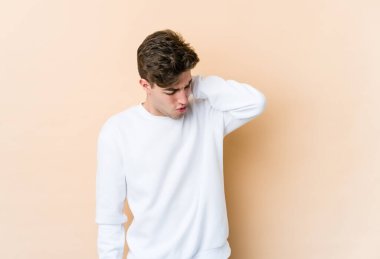 Beyazlı genç bir adam bej arka planda izole edilmiş. Stres yüzünden boynu ağrıyor. Masaj yapıyor ve elle dokunuyor..