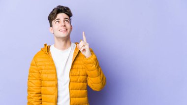 Mor arka planda izole genç beyaz adam iki ön parmağı da boş bir alan gösteriyor..