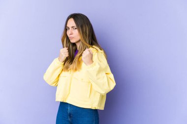 Mor arka planda izole edilmiş genç beyaz kadın yumruğunu kameraya gösteriyor, agresif yüz ifadesi var..