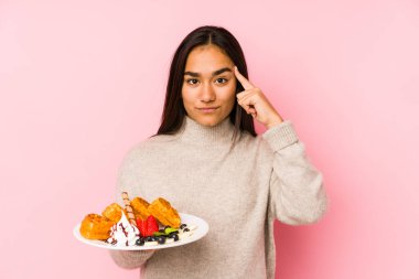 Elinde waffle tutan Asyalı genç bir kadın, bir işaret ile tapınağı işaret ediyor, düşünüyor, bir göreve odaklanıyor..