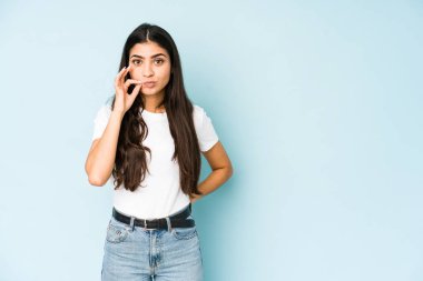 Mavi arka planda, dudakları dudaklarında sır saklayan genç Hintli bir kadın..