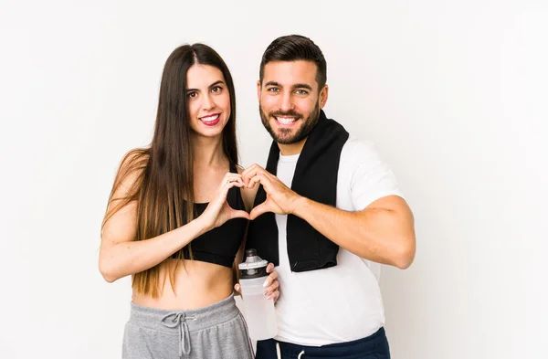 Young caucasian fitness couple isolated smiling and showing a heart shape with hands.