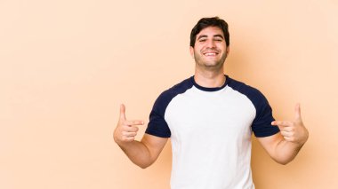Bej arka planda izole edilmiş genç adam parmakları aşağıda, olumlu hisler içinde..