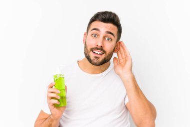 Genç, beyaz bir adam elinde aloe vera ile nemlendirici tutuyor. Dedikoduları dinlemeye çalışıyor..