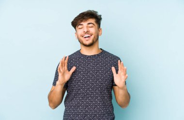 Genç Arap bir adam mavi bir arka planda izole edilmiş neşeli bir şekilde gülüyor. Mutluluk kavramı.