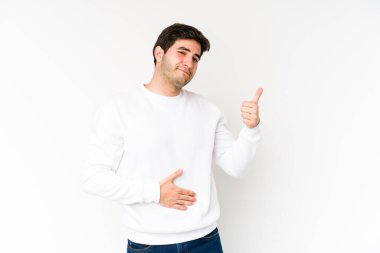 Beyaz arka planda soyutlanmış genç adam karnına dokunuyor, nazikçe gülümsüyor, yemek yiyor ve tatmin oluyor..