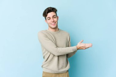 Mavi arka planda izole edilmiş genç beyaz bir adam palmiyesinde bir kopya alanı tutuyor..