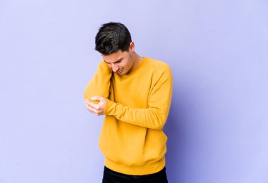 Genç beyaz adam mor arka planda izole edilmiş dirsek masajı yapıyor, kötü bir hareketin ardından acı çekiyor..