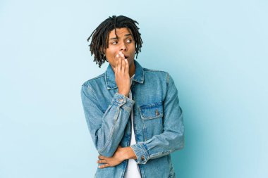 Kot ceket giyen genç siyahi adam esniyor. Ağzı eliyle kapatan yorgun bir hareket sergiliyor..