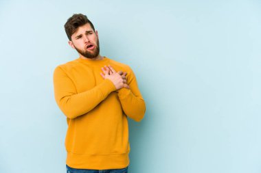 Mavi arka planda izole edilmiş beyaz bir genç, dost bir ifadeye sahip, avuçlarını göğsüne bastırıyor. Aşk konsepti.